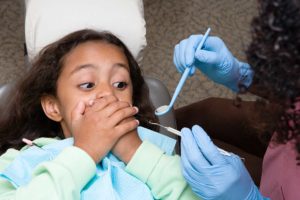 criança no dentista tapando a boca com medo